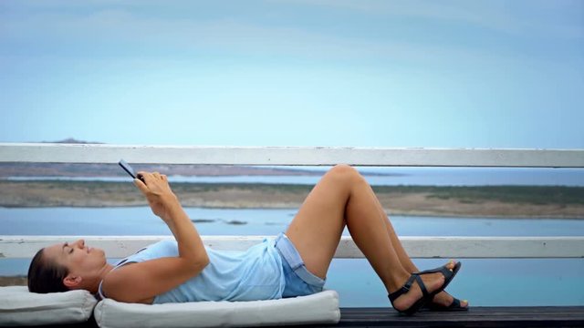 Woman using cellphone while relaxing on outdoor terrace by the sea