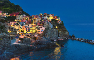 Fototapeta na wymiar Manarola traditional typical Italian village in National park Cinque Terre with colorful multicolored buildings houses on rock cliff and marine harbor, night evening view, La Spezia, Liguria, Italy