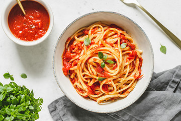 Top view of traditional pasta with tomato and Greek basil sauce in a ceramic bowl on a white table.