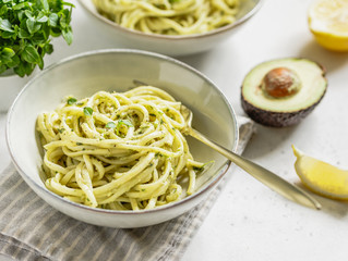 Pasta with avocado and Greek basil sauce in a ceramic bowl on a white table.