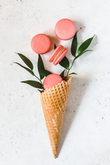 Spring abstract bouquet with a waffle cone, coral macaroons and green plant on a white background. Top view, flat lay.