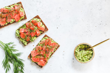 Three toasts with avocado, rye bread, smoked salmon on a white background. Top view, flat lay, copy space.
