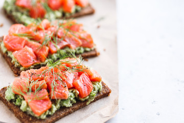 Close-up view of three sandwiches with rye bread, avocado and smoked salmon on a white kitchen table. Copy space.