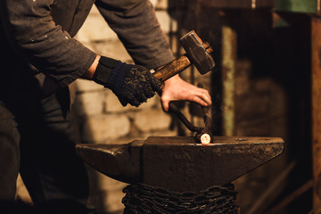 The blacksmith manually forging the red-hot metal on the anvil in smithy.