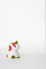 Small cute white unicorn toy with coral hair on a white empty background. Isolated. Copy space. Symbol. Kid. Colour. Vertical