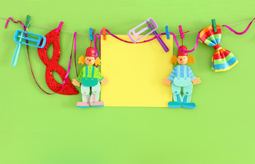 Purim celebration concept (jewish carnival holiday) with empty note for text, clown, mask and noisemaker over wooden green background
