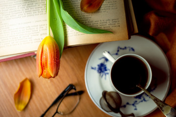 Tulip flowers over vintage books near a cup of tea