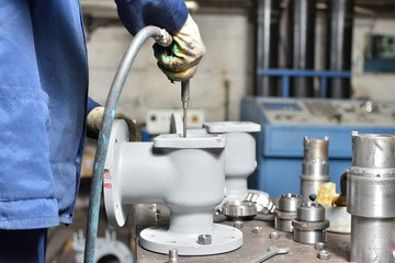 The base for the valve is mounted on an iron table for assembly at the factory and a worker working with high air pressure blows away small debris before assembly.