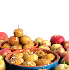 Baked apples in round clay bowls and lot of ripe fresh apples studio shot isolated on white background closeup