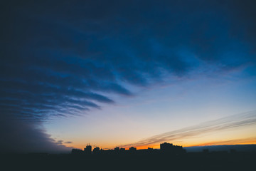 Cityscape with wonderful varicolored vivid dawn. Amazing dramatic blue cloud sky above dark...