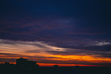Cityscape with wonderful varicolored fiery dawn. Amazing dramatic multicolored cloudy sky. Dark...