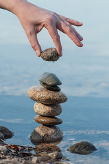 Closeup of man putting pebble on stone balance  in the water of lake with reflection