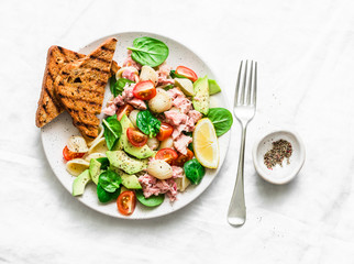Orecchiette pasta, tuna, avocado, spinach, tomato salad and whole grain bread toast - delicious healthy lunch on a light background, top view