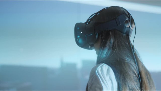 A young girl-client studies a design project in virtual reality glasses, looks around. Close-up, projection on the wall. The future of architecture and construction industry. Loft-office. Red epic. 4K