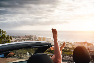 View of woman legs inside convertible car during a road trip - Young girl having fun traveling in cabriolet car in summer vacation - People, travel and youth lifestyle concept - obrazy, fototapety, plakaty