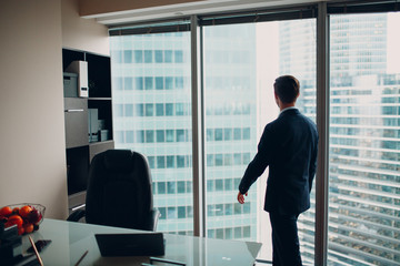 Fototapeta premium A young man in a skyscraper office is standing by a panoramic window.