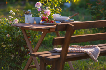 Morning tea in the garden. Fresh roses on wooden table, sunny day, natural ligh