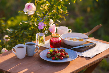 Morning tea in the garden. Fresh roses on wooden table, sunny day, natural ligh