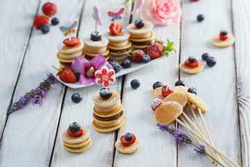 Fruit, berry and pancake canapes on white wooden table