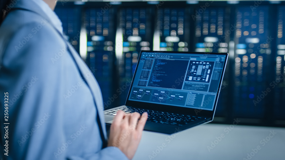 Poster back view close up shot of an it specialist working on laptop in data center next to server racks. c