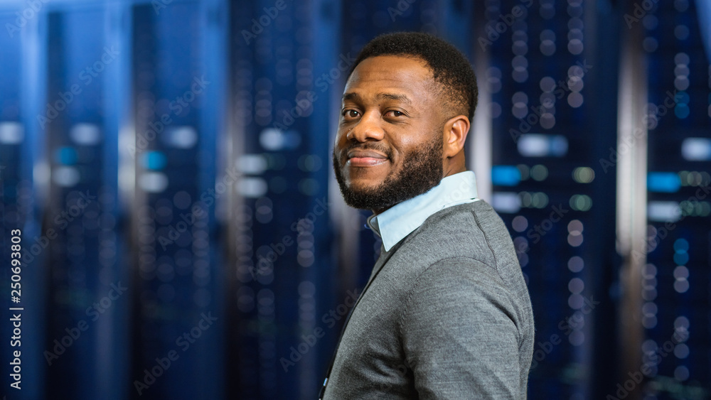Poster Young Black Data Center IT Technician Standing in Server Rack Corridor and Smiling to the Camera.