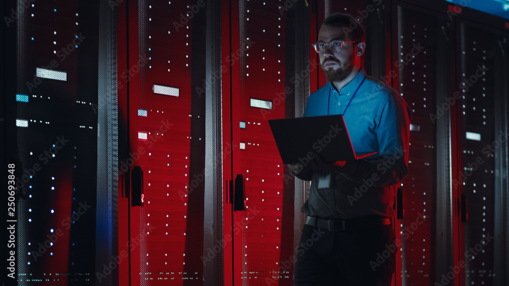 Poster angry bearded it specialist in glasses is walking through server rack corridor in data center and ho
