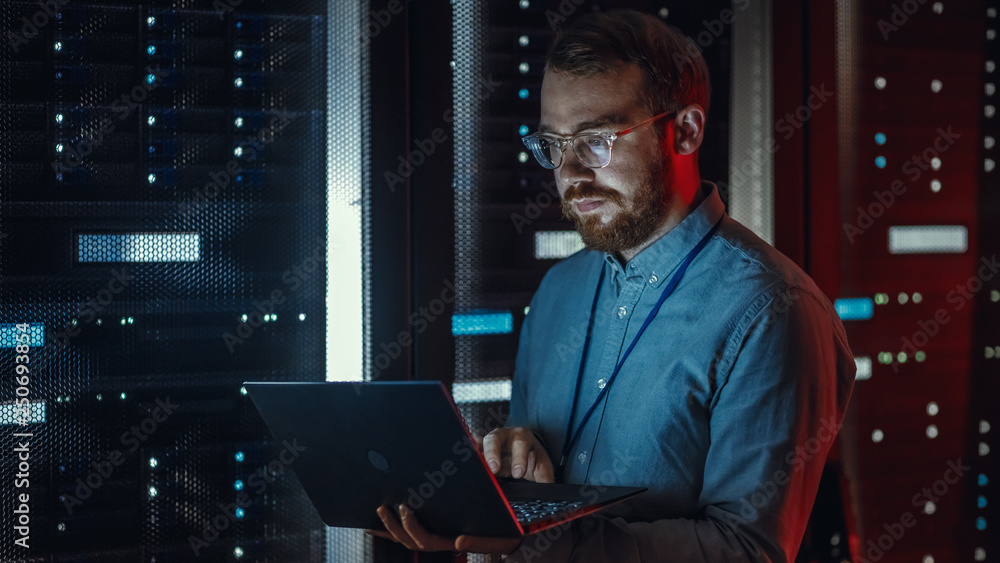 Aufkleber bearded it specialist in glasses is working on laptop in data center while standing near server rack