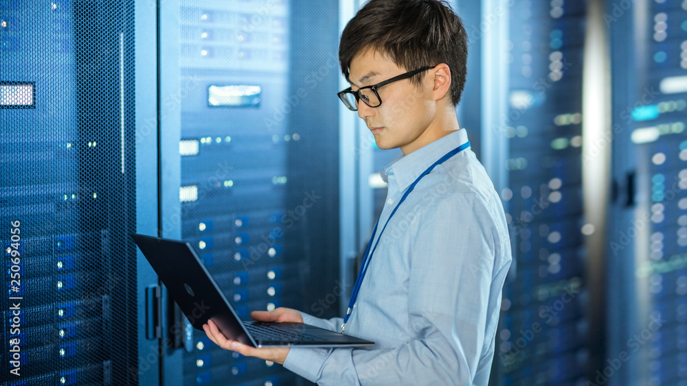 Poster in the modern data center: it engineer standing beside server rack cabinets, does wireless maintenan