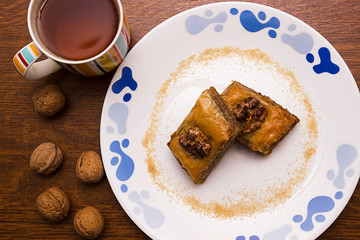 Baklava on a white plate, cup with tea, walnuts