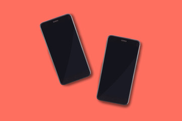Pair of black slim smartphones in center on background of coral color. Top view