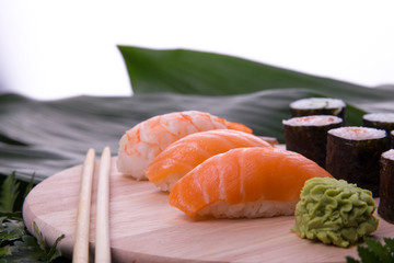 set of sushi on a wooden board with leaves of plants on a dark background