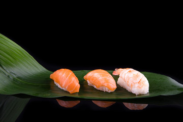 set of sushi on a wooden board with leaves of plants on a dark background