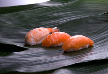 set of sushi on a wooden board with leaves of plants on a dark background