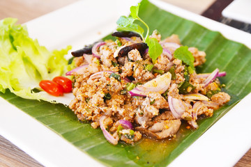 spicy minced pork salad on the banana leaf decorated white plate (Larb Moo)