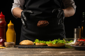 Chef puts beef patty on a burger loaf, against the background of the ingredients. Delicious and harmful food, fast food, homemade recipes, restaurant, catering, recipe book