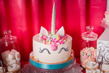 Sweet table and big unicorn cake for baby girl first birthday. Candy bar with a lot of different candies and sweet cakes