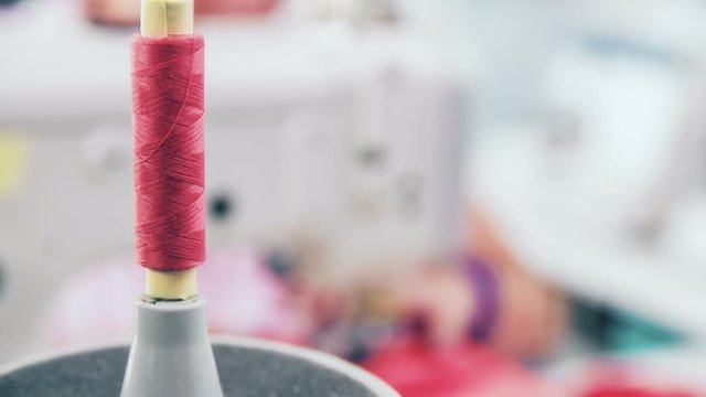 Professional seamstress working. Jib shot close-up on a pink thread and refocus to seamstress sewing on the machine.