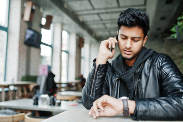 Portrait of stylish and casual young asian man wear on leather jacket spending time at cafe, speaking on mobile phone and looking at watches.