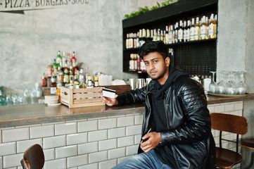 Casual and stylish young asian man wear on leather jacket sitting on bar and holding credit card for pay.