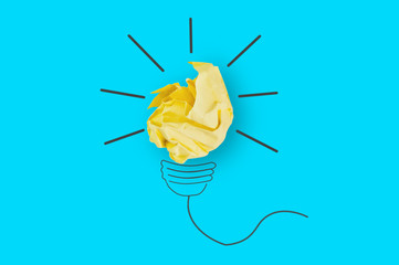 One crumpled yellow paper and image on blue table in office made light bulb. Top view. Inspiration concept