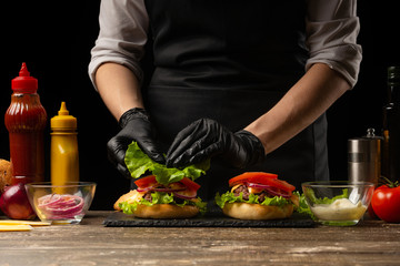 The chef lays out a fresh salad on a burger, with ingredients in the background. Horizontal photo, Tasty and unhealthy food, fast food, homemade recipes, restaurant, catering, recipe book