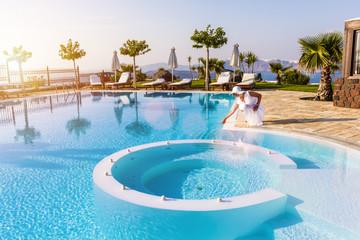 Elegant woman touching the water in a swimming pool. Sunset light, soft focus,best  focus at the woman