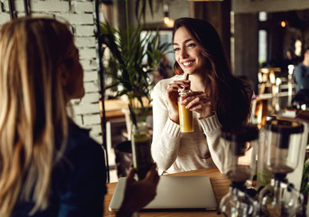 Happy woman enjoying in conversation with her friend and drinking smoothie.