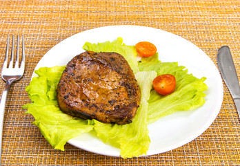 Steak meat with tomato and lettuce salad leaf and fork in a white plate