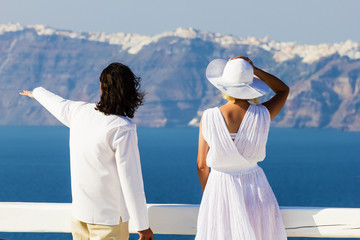 Elegant couple on the vacation at Santorini island, Greece. Rear view, man pointing at panorama of island