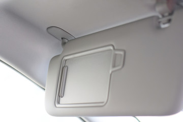 Car visor. Car interior. Grey open sun car visor with selective focus and car mirror on blurred background with automobile window