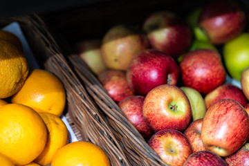 Closeup of many red apples and oranges in baskets at farmer's market shop store showing detail and texture assortment