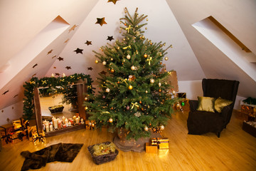 Christmas decorations in the studio, big natural fir tree with golden balls, bows and snowflakes, wooden fireplace and candles on it and brown cozy armchair