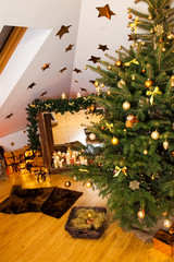 Christmas decorations in the studio, big natural fir tree with golden balls, bows and snowflakes, wooden fireplace and candles on it and brown cozy armchair