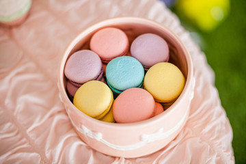 Candy bar for the first birthday for little baby girl. Sweet table and nice pink, blue, purple, yellow macaroons in the round pink box on the light pink table.